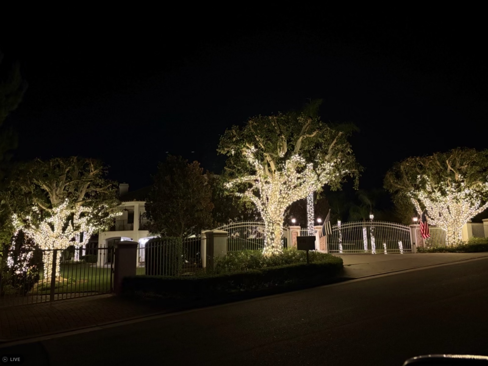 Gated estate with two large light-wrapped specimen trees and a US flag