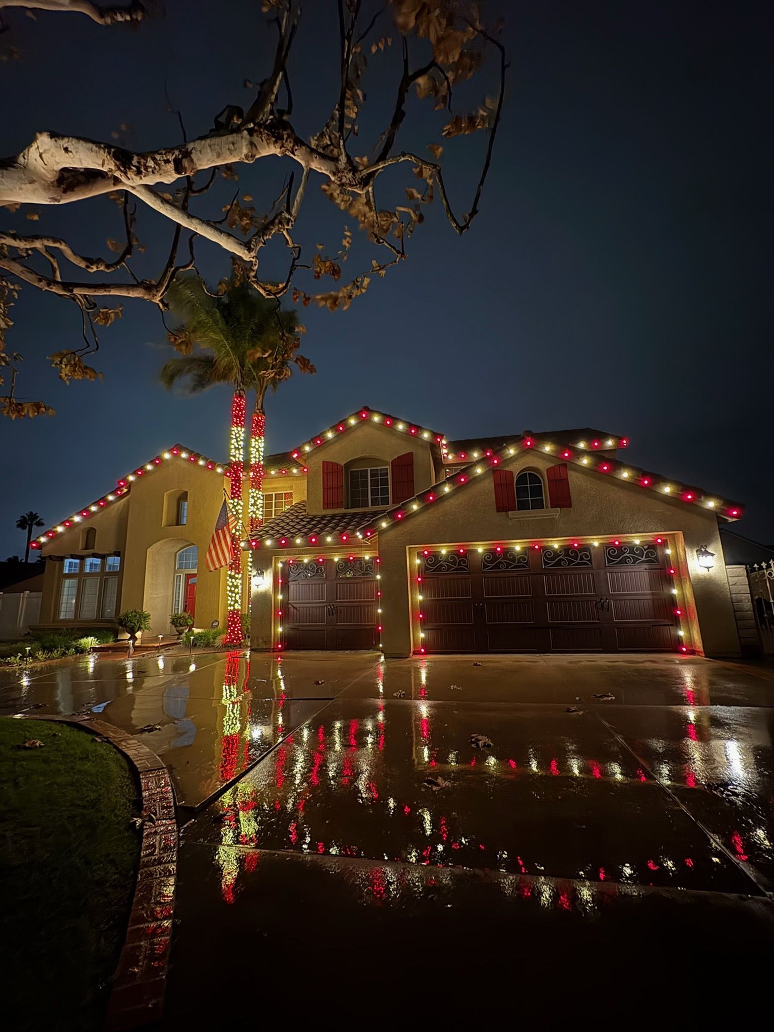 Red and warm white roofline and garage outlines reflecting in a rain-wet driveway
