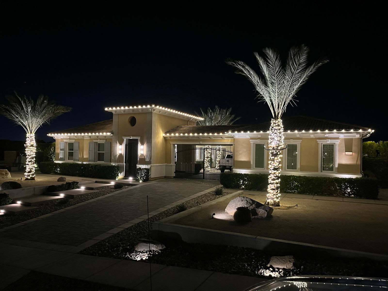 Single-story Mediterranean home with warm white roofline and lit palm wraps